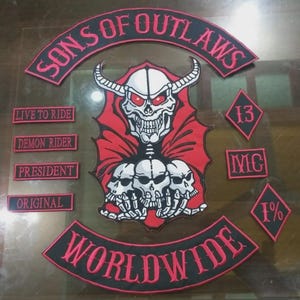 May include: A collection of embroidered patches with a biker theme. The central patch features a skull with horns and red eyes, surrounded by the words "SONS OF OUTLAWS" and "WORLDWIDE". Additional patches include "LIVE TO RIDE", "DEMON RIDER", "PRESIDENT", "ORIGINAL", "13", "MC", and "1%."