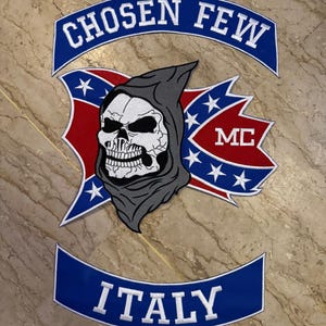 Puede incluir: Un parche con las palabras "CHOSEN FEW" en blanco sobre una pancarta azul. El parche presenta una calavera con una capucha gris, con el texto "MC" en rojo. La palabra "ITALY" está en blanco sobre una pancarta azul.