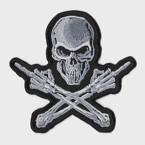 Könnte beinhalten: Gestickter Aufnäher mit einem Totenkopf und gekreuzten Skeletthänden. Der Schädel und die Hände sind grau, mit schwarzer Umrandung und schwarzem Hintergrund. Der Aufnäher ist wahrscheinlich für Jacken, Taschen oder andere Kleidungsstücke.