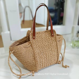 Puede incluir: Un bolso tote de ganchillo beige con un patrón tejido texturizado, que cuenta con dos asas de cuero marrón sujetas con remaches metálicos y finos lazos laterales de ganchillo. El texto RUETHAI y Terra Trio Crochet Bag Pattern PDF Digital Download es visible.