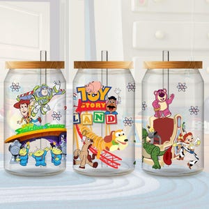 May include: Three clear glass beverage cups with wooden lids and straws. Each cup features a different Toy Story character design. The first cup has Buzz Lightyear, Woody, and the aliens. The second cup has the Toy Story Land logo and characters. The third cup has Lotso, Rex, and Jessie.