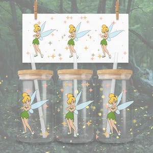 May include: Three glass tumblers with wooden lids and straws, each featuring a cartoon image of a fairy with blonde hair, green dress, and blue wings. A matching print with the same fairy design is displayed above the tumblers.