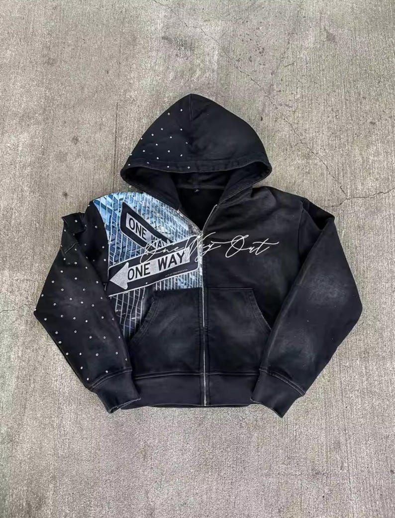 May include: Black zip-up hoodie with a hood and front pocket. The left side features a street sign graphic with "ONE WAY" text, while the right side has the text "Go Out". The hood is embellished with small, silver studs.