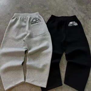 Puede incluir: Se muestran dos pares de pantalones de ch&aacute;ndal, uno gris y otro negro. Cada par tiene un bolsillo trasero con un peque&ntilde;o gr&aacute;fico circular. Los pantalones de ch&aacute;ndal tienen un corte holgado y una cintura con cord&oacute;n.