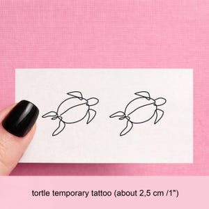 May include: Two minimalist black line art turtle temporary tattoos on a white card, set against a pink backdrop. The card includes the text "tortle temporary tattoo (about 2.5 cm)".