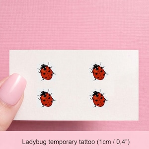 May include: A white rectangular sheet featuring four identical ladybug temporary tattoos, each with a red body, black spots, and a black head. The text on the sheet indicates a size of 0.4 inches for each individual ladybug temporary tattoo.