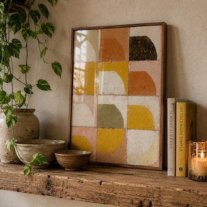 Peut inclure: Une œuvre d'art murale encadrée rectangulaire composée d'une grille de douze carreaux carrés. Chaque carreau présente un motif géométrique de demi-cercle de couleur unie dans des tons jaune moutarde, orange terre cuite, vert olive et crème sur fond neutre.