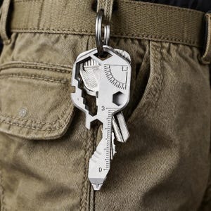 May include: A multi-tool key with a silver finish hangs from a key ring attached to a belt loop. The key features various cut-out shapes, a ruler with inch measurements, and a bottle opener. The key is shown against a khaki-colored background.