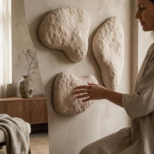 Puede incluir: Tres piezas de arte mural abstractas y texturizadas en un color beige neutro. Las formas orgánicas están montadas en una pared de color claro, creando una estética minimalista y moderna. Las piezas de arte son de diferentes tamaños y formas, agregando interés visual.