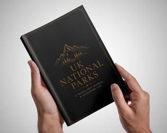 May include: A black journal with gold lettering that reads UK NATIONAL PARKS A TRAVELLER'S JOURNAL & ADVENTURE LOG. The cover features a gold line-art illustration of mountain peaks and a thin gold border frame around the edges of the book.