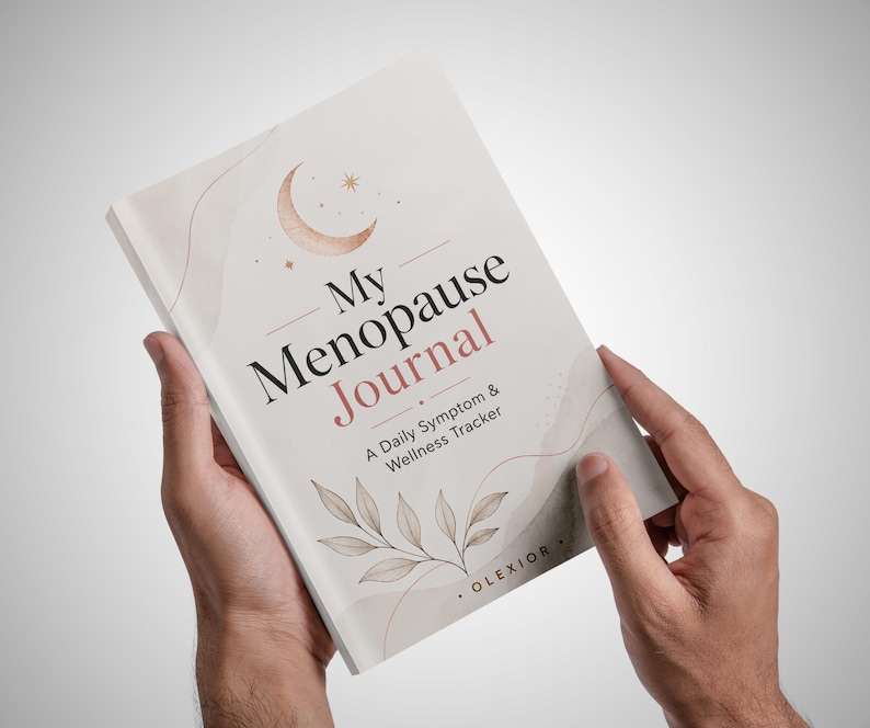 May include: A softcover book titled My Menopause Journal: A Daily Symptom & Wellness Tracker. The cover is off-white with a rose gold crescent moon, stars, and leaf illustrations. The text OLEXIOR is printed at the bottom right corner.