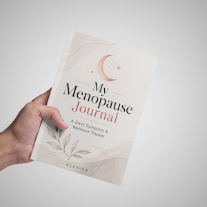 May include: A softcover journal with a cream-colored cover featuring a crescent moon, botanical illustrations, and the text My Menopause Journal: A Daily Symptom & Wellness Tracker by Olexior. The design includes muted pink and brown accents.