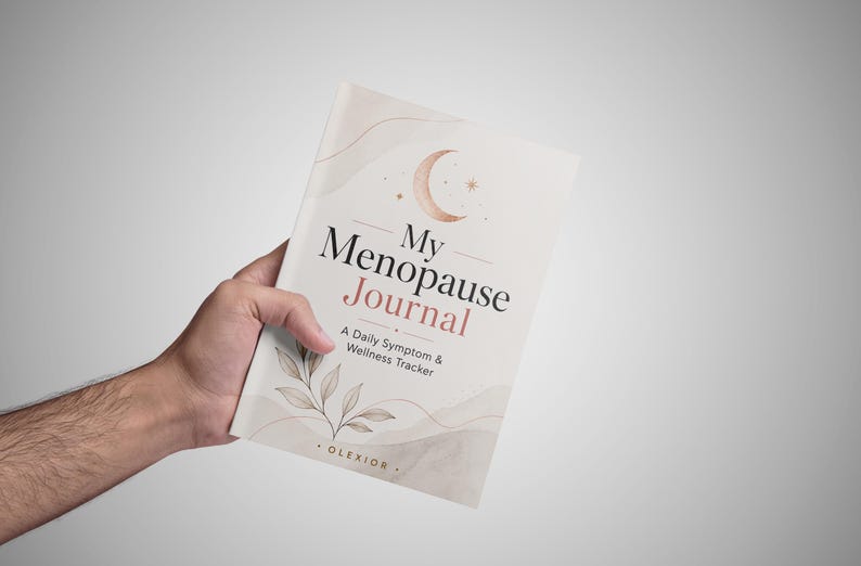May include: A softcover journal with a cream-colored cover featuring a crescent moon, botanical illustrations, and the text My Menopause Journal: A Daily Symptom & Wellness Tracker by Olexior. The design includes muted pink and brown accents.