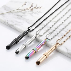 Puede incluir: Cuatro silbatos cilíndricos de metal unidos a cadenas de eslabones cuadrados a juego. Los silbatos tienen acabados en negro mate, plata pulida, arcoíris iridiscente y oro cepillado. Cada silbato cuenta con un anillo de agarre texturizado.
