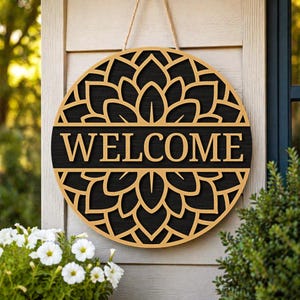 May include: Round wooden welcome sign with a floral design and the word "WELCOME" in a bold font. The sign is made of dark wood with a light wood border and is hanging by a natural rope.