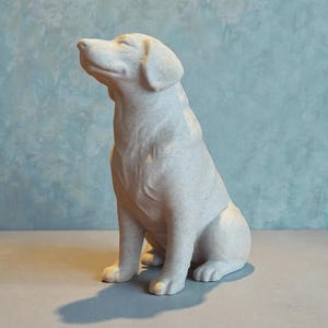 Op de afbeelding: Een zittend, gebroken wit hondenbeeld met een serene uitdrukking. De sculptuur heeft een textuur en staat tegen een lichtblauwe achtergrond. De hond zit rechtop, met zijn hoofd omhoog gekanteld.