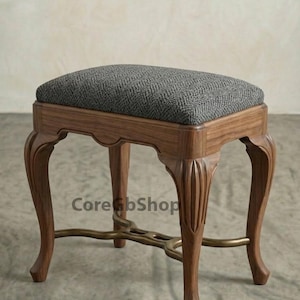 May include: A wooden vanity stool with a gray upholstered seat. The stool has curved legs and a decorative brass support. The seat cushion is approximately 18 inches wide and 14 inches deep.