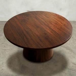 May include: A round, dark brown wooden coffee table with a pedestal base. The table has a smooth, polished surface and is approximately 30 inches in diameter. The base is a solid, cylindrical shape. The table is set against a neutral background.