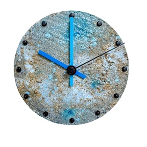 May include: Round wall clock with a textured, blue, and tan face. The clock has black hour markers and blue hands. The clock's face has a unique, weathered appearance. The clock is a decorative item.