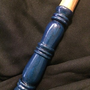 May include: A wooden wand with a dark blue painted handle. The handle has a textured design with multiple rings.