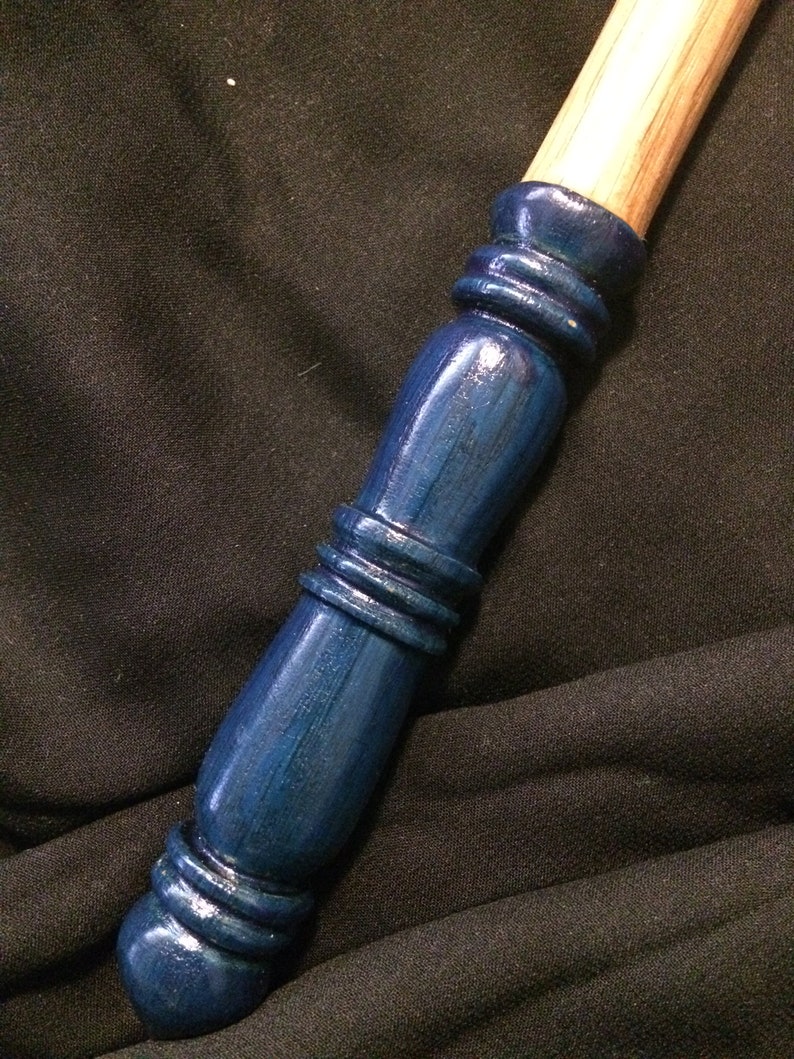 May include: A wooden wand with a dark blue painted handle. The handle has a textured design with multiple rings.