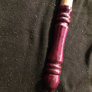 May include: A wooden wand with a dark purple, glossy finish. The wand has a rounded tip and a series of decorative rings near the end.