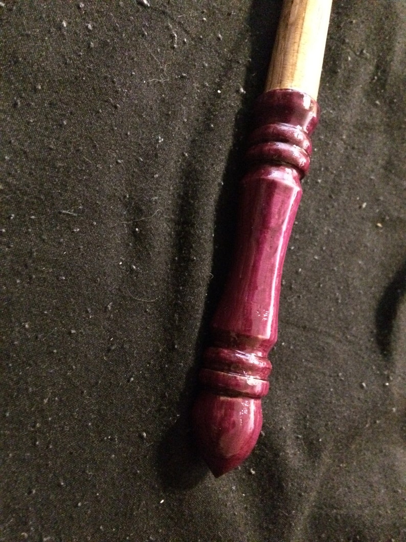 May include: A wooden wand with a dark purple, glossy finish. The wand has a rounded tip and a series of decorative rings near the end.