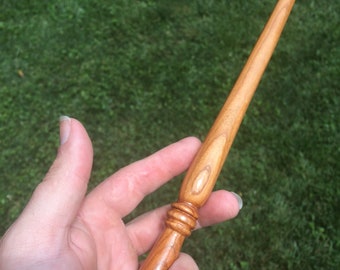 May include: A wooden wand with a brown finish and a rounded tip. The wand has a decorative knob near the handle.
