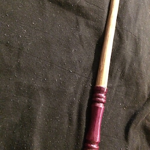 May include: A wooden wand with a dark burgundy painted handle. The wand is approximately 30 cm long.