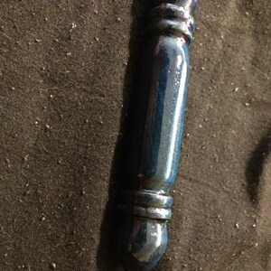May include: A wooden wand with a dark blue, glossy finish. The wand has a rounded tip and two silver bands near the end.