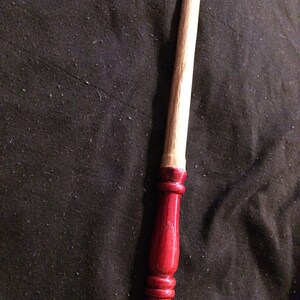 May include: A wooden wand with a red painted tip. The wand is approximately 30 cm long and has a smooth, polished finish.