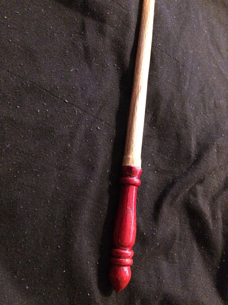 May include: A wooden wand with a red painted tip. The wand is approximately 30 cm long and has a smooth, polished finish.
