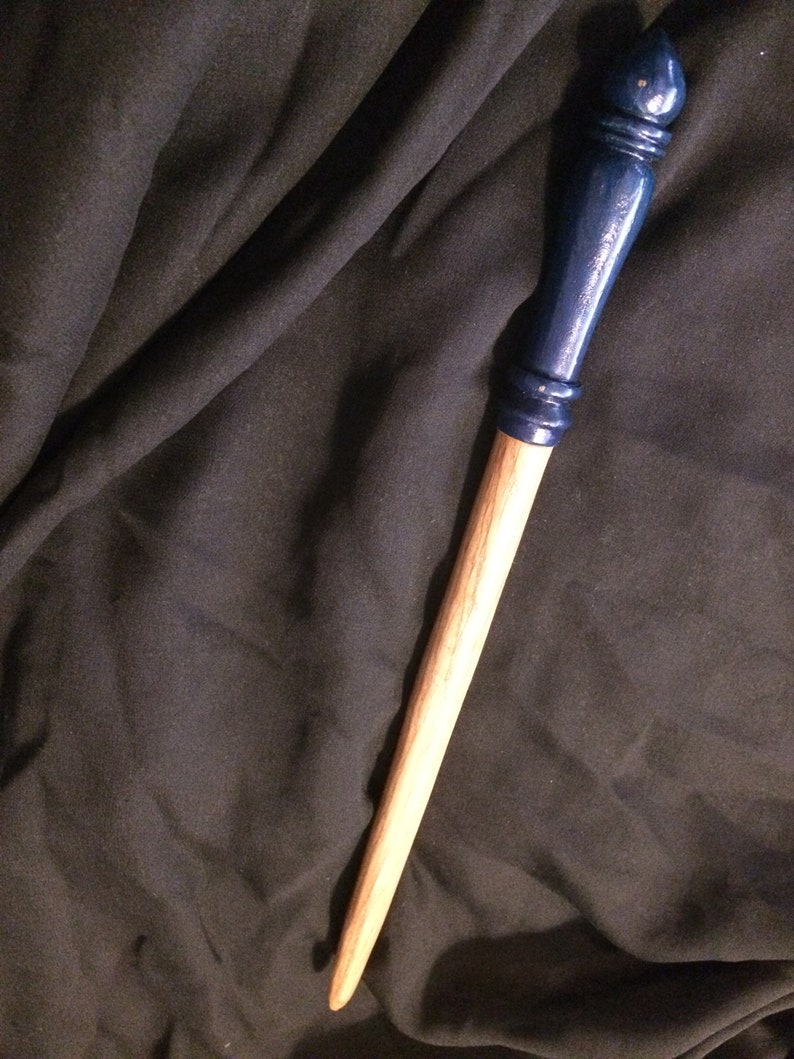 May include: A wooden wand with a dark blue painted tip. The wand is approximately 30 cm long and has a smooth, natural finish.