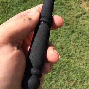 May include: A black wooden wand with a pointed tip and a decorative knob at the top.