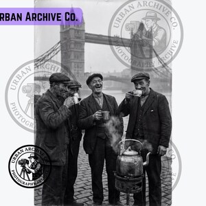 May include: A black and white photograph featuring three individuals wearing flat caps and dark jackets, standing outdoors near a steaming metal kettle on a portable stove. They are holding small metal cups. Tower Bridge is visible in the background.