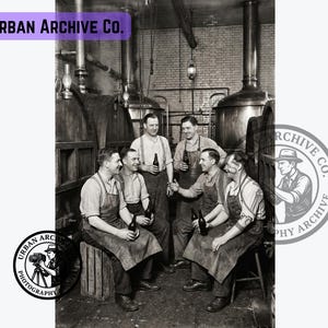 Pode incluir: Uma fotografia histórica a preto e branco intitulada Urban Archive Co. mostrando cinco pessoas com aventais de trabalho dentro de uma cervejaria. Estão reunidas em torno de grandes barris de madeira e cubas de metal, cada uma segurando uma garrafa de vidro escuro. A cena captura um momento de camaradagem num ambiente industrial com paredes de tijolo e lanternas suspensas.