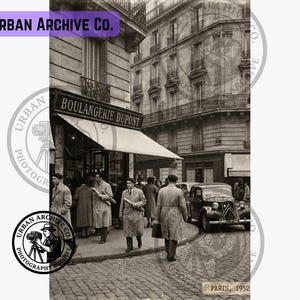 May include: A black and white photograph titled Paris, 1952, showing a street scene with a storefront labelled Boulangerie Dupont. People in long coats walk on a cobblestone street near a vintage car. The image includes the text Urban Archive Co.