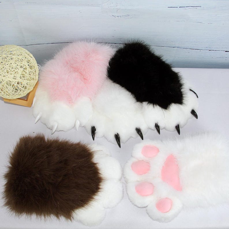 May include: A selection of plush paw-shaped accessories in various colours. The paws feature white, pink, black, and brown fur with black claws and pink paw pads. These items are likely designed for cosplay or costume use.