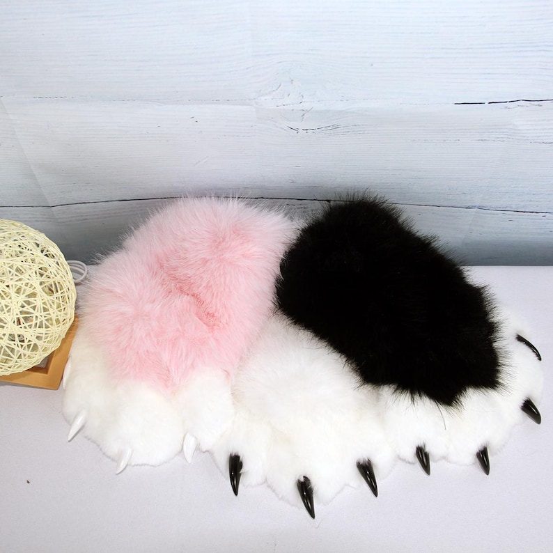 May include: Fluffy paw-shaped slippers in pink, black, and white. The slippers have long, soft fur and sharp black claws. The slippers are designed to look like animal paws.