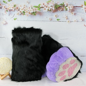 May include: Black faux fur boots with purple paw pads and pink paw prints. The boots are designed to resemble animal paws. The boots are a unique costume accessory.
