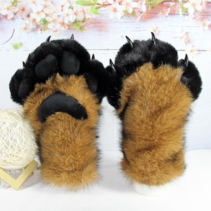 May include: A pair of plush animal paw gloves featuring long brown faux fur on the back and black faux fur on the fingers. The palms are covered in black fabric with padded paw pads and pointed black plastic claws attached to each finger tip.
