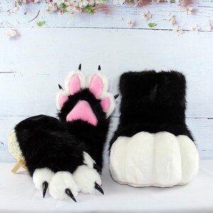 May include: A pair of black and white furry paw gloves and a matching foot covering. The gloves have pink paw pads and black claws. The foot covering is white with black fur on top.