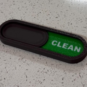 May include: A black rectangular sliding indicator sign with rounded edges. The sign features a green insert with the word CLEAN printed in white capital letters. A black sliding cover is positioned over the left side of the indicator.