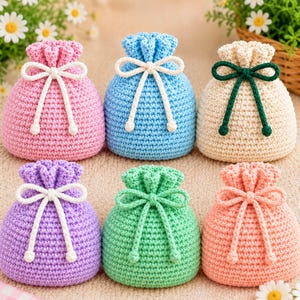 Puede incluir: Seis pequeñas bolsas redondas de ganchillo con cordón en rosa, azul claro, crema, morado, verde menta y melocotón. Cada bolsa presenta un patrón de punto texturizado y un cordón a juego o en contraste atado en un lazo en la parte superior.