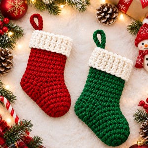 May include: Two crochet Christmas stockings, one in solid red and one in solid green, each featuring a thick white cuff and a matching yarn hanging loop at the top. The stockings are crafted with a textured stitch pattern and are displayed together.