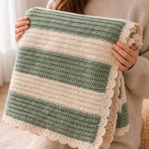May include: A rectangular crochet blanket featuring alternating horizontal stripes in sage green and cream. The blanket is constructed with a textured ribbed stitch pattern and is finished with a decorative scalloped edge border in cream.