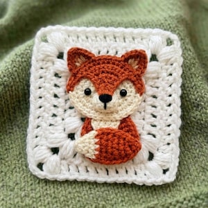 Könnte beinhalten: Gehäkeltes Quadrat mit einem 3D-Fuchs-Motiv. Der Fuchs ist in Orange- und Cremetönen mit schwarzen Augen gehalten und auf einem weißen, gehäkelten Quadrat platziert. Geeignet für Bastelarbeiten oder als Dekoration.