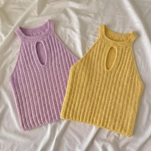 May include: Two sleeveless crochet tops, one in light purple and one in yellow. Each top features a high neckline with a vertical oval cutout in the center and a ribbed texture throughout the fabric, creating a consistent pattern across both garments.