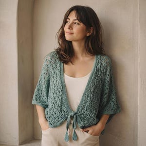 Puede incluir: Una taza de cerámica blanca con asa negra y el texto "But First, Coffee" en negrita negra. La taza se encuentra sobre un fondo borroso, sugiriendo un ambiente acogedor.