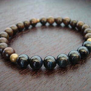 May include: A stretch bracelet with a mix of dark brown, bronze, and black beads. The bracelet features a few gold-coloured beads. The beads are round and smooth, creating a simple, elegant design.